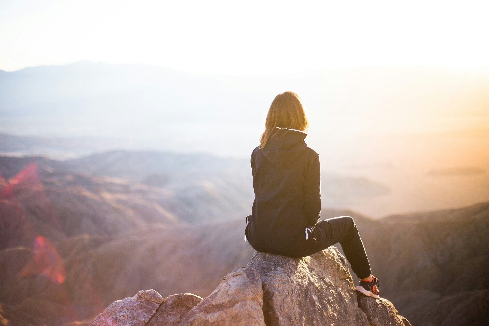 Das Bild zeigt eine junge Frau auf einem Berggipfel sitzend.